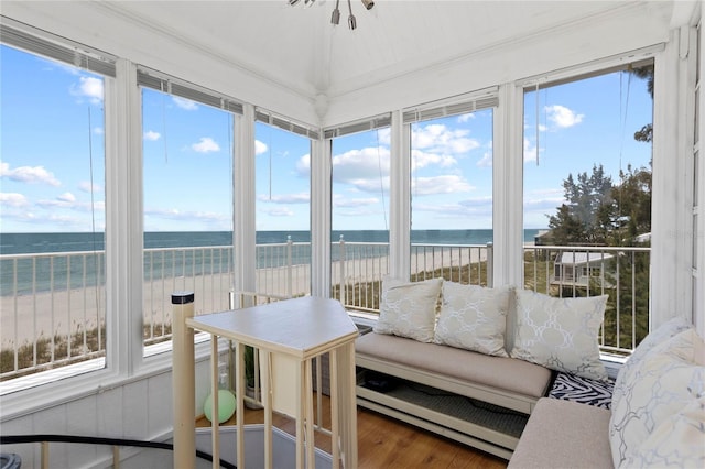 sunroom / solarium featuring vaulted ceiling, a healthy amount of sunlight, a view of the beach, and a water view