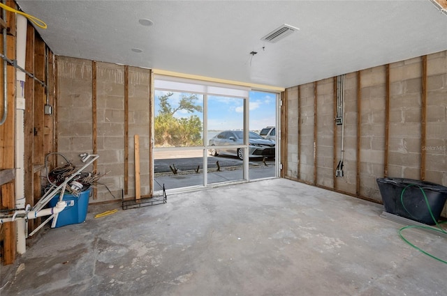 empty room with concrete flooring, concrete block wall, and visible vents