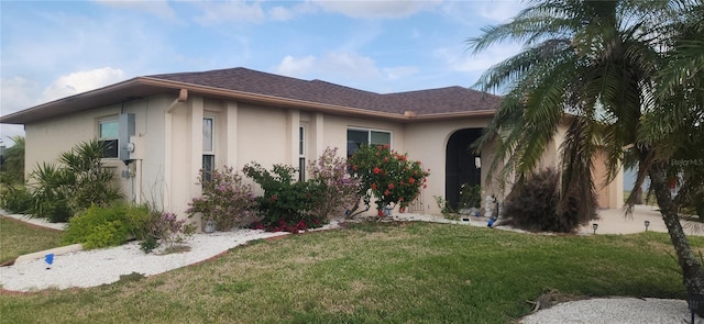 view of front of property featuring a shingled roof, a front yard, and stucco siding