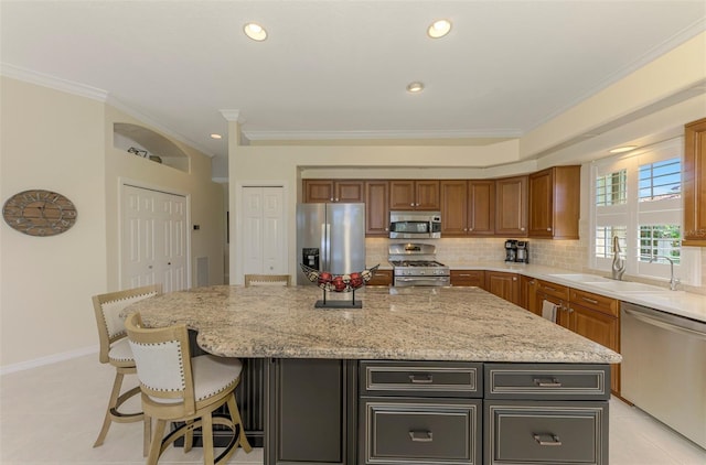 kitchen with a sink, stainless steel appliances, crown molding, decorative backsplash, and light stone countertops