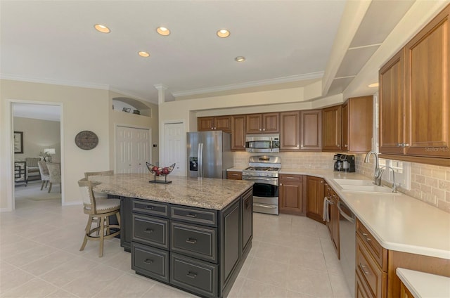 kitchen featuring a breakfast bar, a sink, a center island, stainless steel appliances, and brown cabinetry