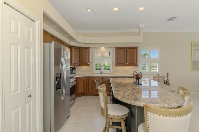 kitchen with visible vents, appliances with stainless steel finishes, a kitchen bar, brown cabinets, and a center island