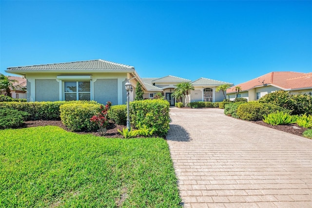 view of front of house featuring decorative driveway, a front lawn, stucco siding, and a tile roof