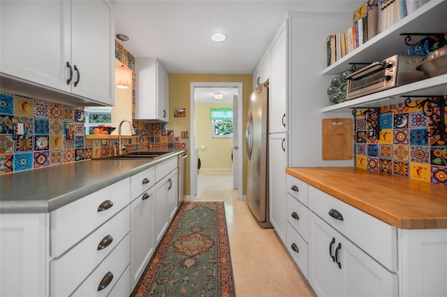 kitchen with decorative backsplash, white cabinets, stainless steel appliances, open shelves, and a sink