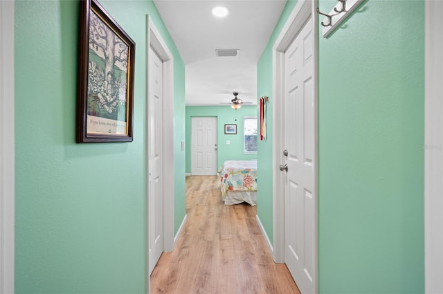 corridor with light wood-type flooring, baseboards, and visible vents