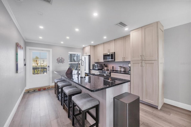 kitchen with light wood finished floors, a center island with sink, visible vents, appliances with stainless steel finishes, and a kitchen bar