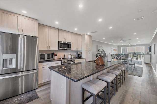 kitchen featuring light wood-style flooring, a kitchen island with sink, stainless steel appliances, a sink, and a kitchen bar