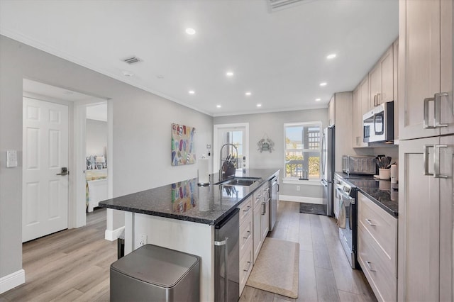 kitchen with light wood-style flooring, stainless steel appliances, a sink, a center island with sink, and crown molding