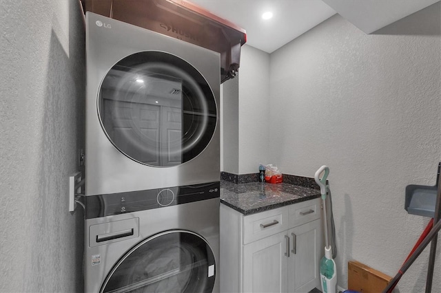 clothes washing area featuring cabinet space, stacked washer / dryer, and a textured wall