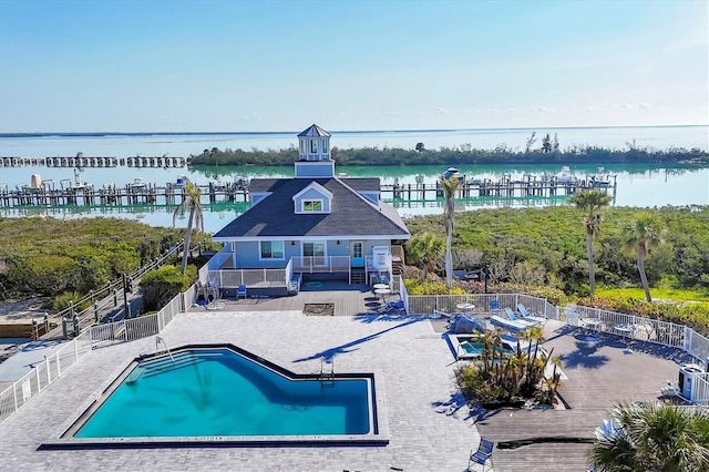 community pool with a patio area, a water view, fence, and stairs