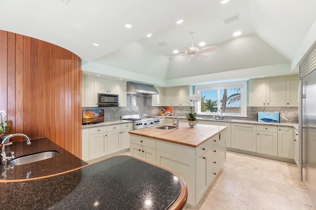 kitchen featuring butcher block countertops, vaulted ceiling, a sink, and wall chimney range hood