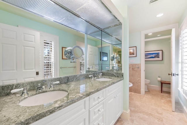 full bath with baseboards, a sink, toilet, and double vanity