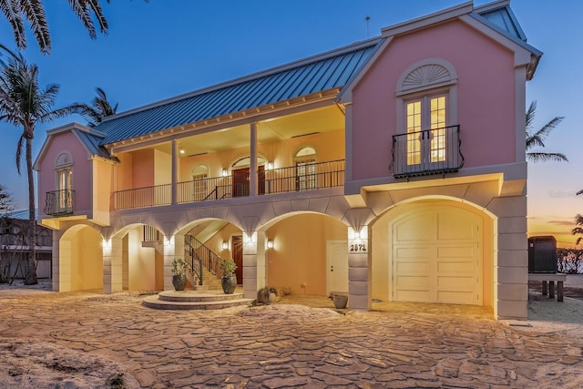 view of front of house featuring a garage, a balcony, metal roof, french doors, and stucco siding