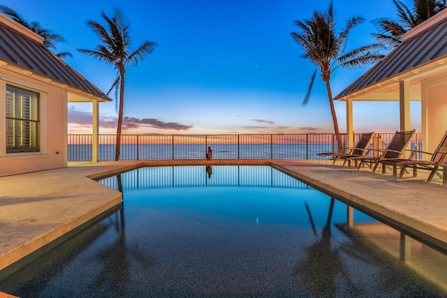 pool at dusk with a fenced in pool, a water view, and a patio