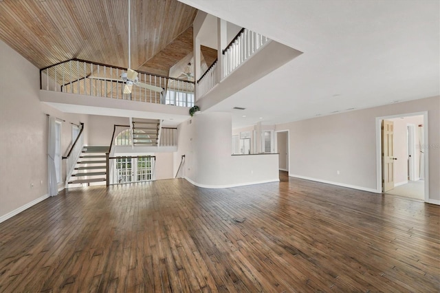 unfurnished living room with a towering ceiling, hardwood / wood-style flooring, wood ceiling, and baseboards