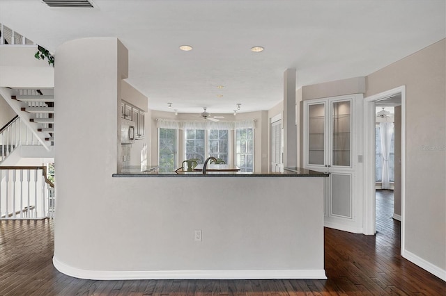 kitchen with stainless steel microwave, dark wood-type flooring, glass insert cabinets, a peninsula, and baseboards