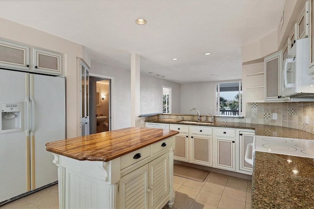 kitchen with light tile patterned floors, wooden counters, decorative backsplash, a sink, and white appliances