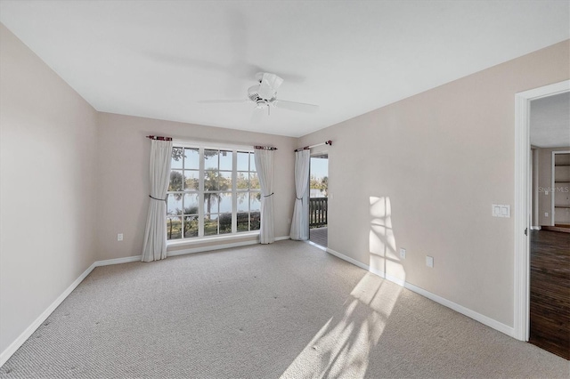 carpeted spare room with a water view, ceiling fan, and baseboards