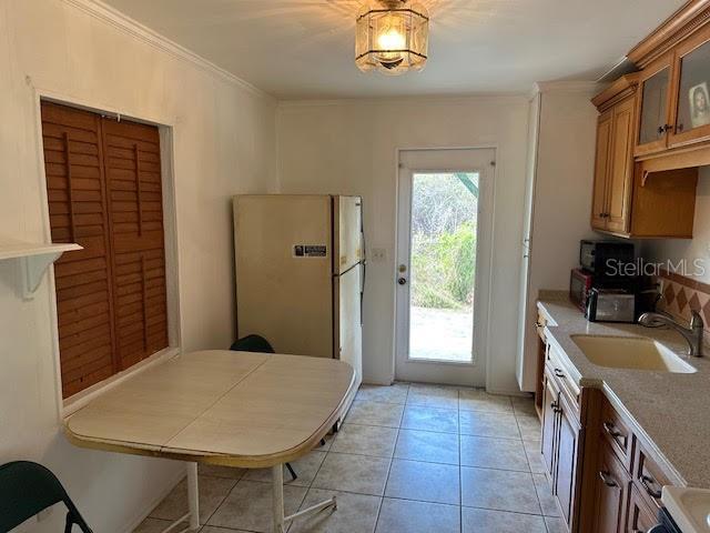 1417 Terry Ave, Punta Gorda, FL 33980 - kitchen with brown cabinetry, freestanding refrigerator, glass insert cabinets, ornamental molding, and a sink