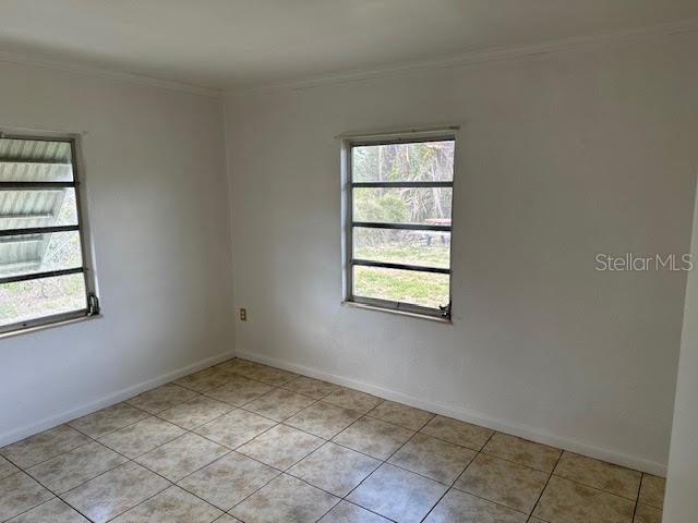 1417 Terry Ave, Punta Gorda, FL 33980 - empty room featuring light tile patterned floors, plenty of natural light, baseboards, and crown molding