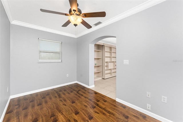 spare room featuring visible vents, wood finished floors, arched walkways, crown molding, and baseboards