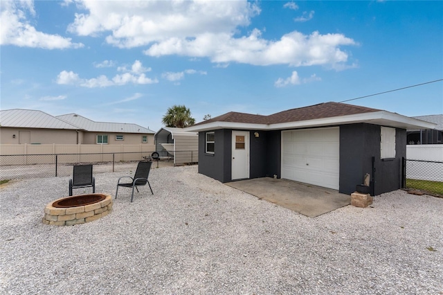 exterior space with stucco siding, an outdoor fire pit, fence, gravel driveway, and an attached garage