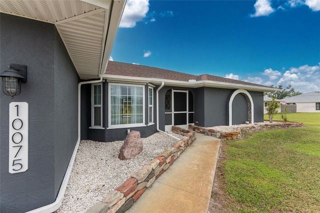 exterior space with a shingled roof, a lawn, and stucco siding