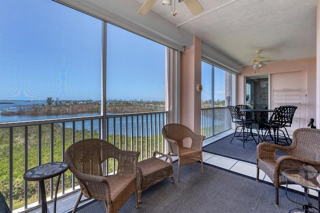 sunroom with ceiling fan and a water view