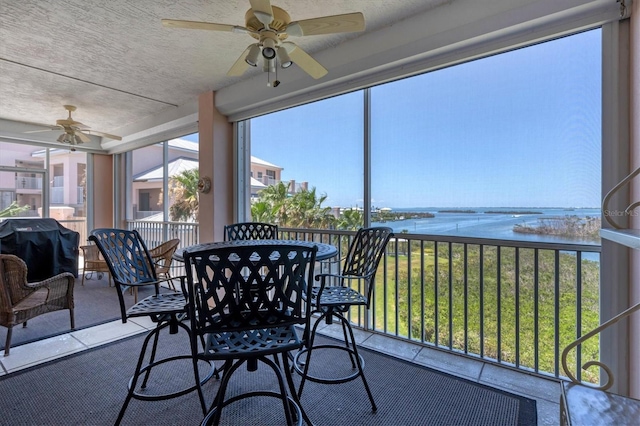 sunroom / solarium featuring a water view, plenty of natural light, and ceiling fan