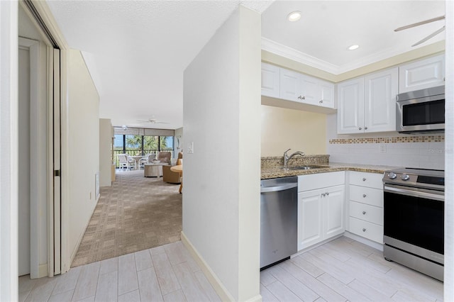 kitchen featuring tasteful backsplash, light stone counters, appliances with stainless steel finishes, white cabinetry, and a sink