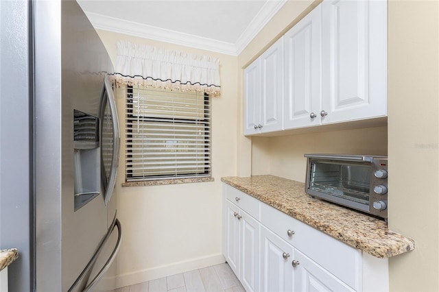 kitchen featuring light stone counters, ornamental molding, white cabinetry, stainless steel fridge, and baseboards