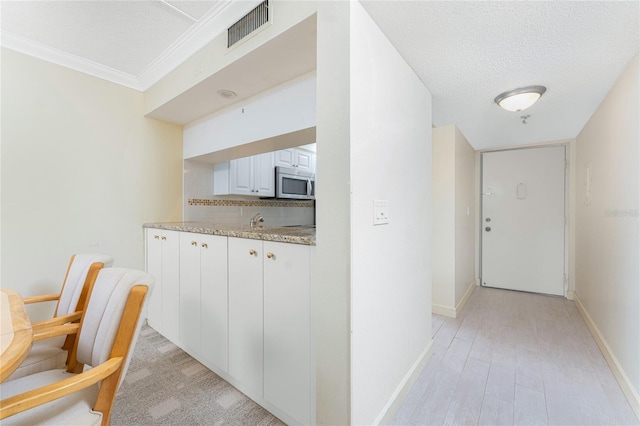 hallway featuring visible vents, ornamental molding, a sink, a textured ceiling, and baseboards