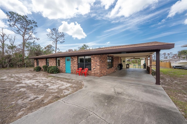 view of front of house featuring brick siding, fence, a carport, and concrete driveway