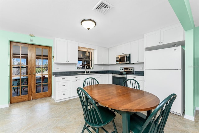 kitchen featuring visible vents, white cabinets, dark countertops, stainless steel appliances, and a sink