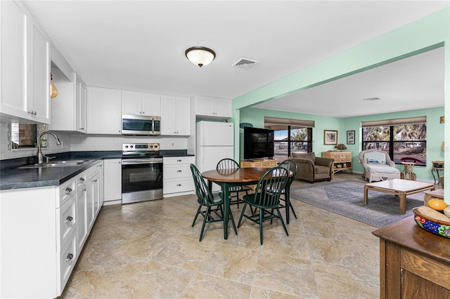 kitchen with white cabinets, dark countertops, a sink, stainless steel appliances, and backsplash