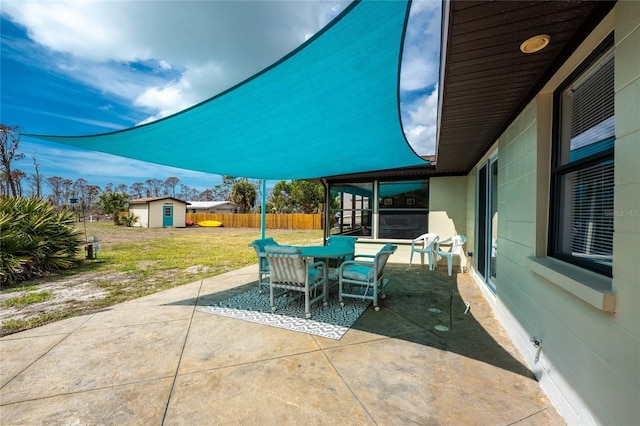 view of patio / terrace with an outbuilding, a storage unit, fence, a sunroom, and outdoor dining space