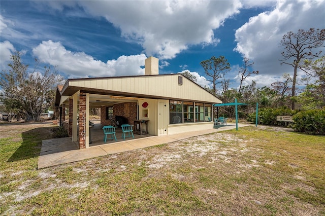 rear view of house featuring a patio area, a lawn, and a chimney