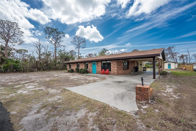 view of front of home with an attached carport, brick siding, an outdoor structure, driveway, and a shed