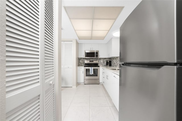 kitchen with light tile patterned floors, tasteful backsplash, light countertops, appliances with stainless steel finishes, and white cabinets