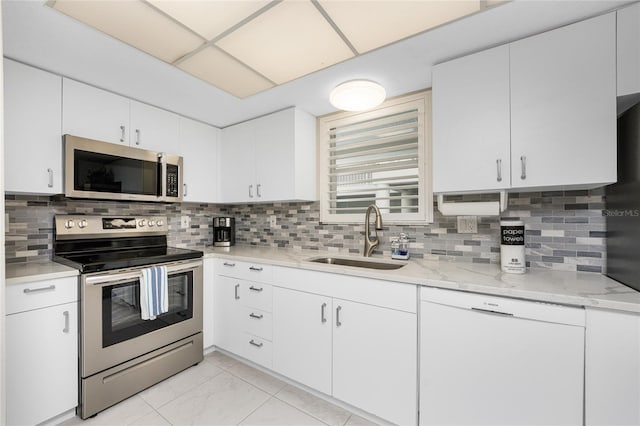 kitchen featuring tasteful backsplash, white cabinets, appliances with stainless steel finishes, light stone countertops, and a sink