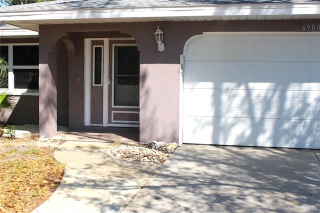 entrance to property featuring driveway, roof with shingles, and stucco siding