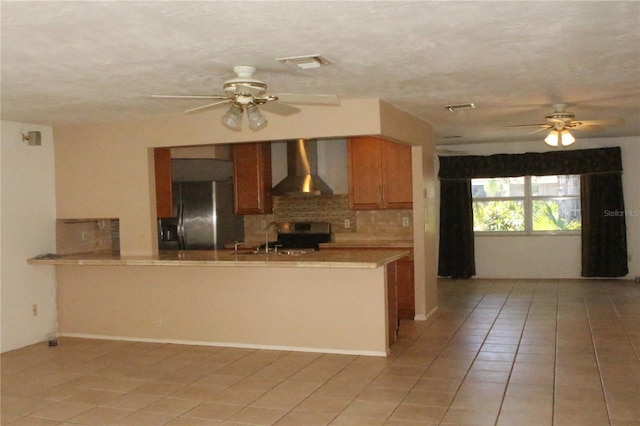 kitchen featuring a ceiling fan, freestanding refrigerator, decorative backsplash, light countertops, and wall chimney range hood