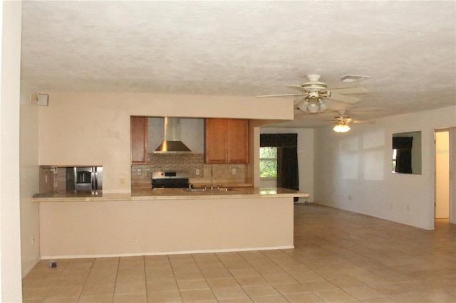 kitchen with brown cabinetry, a sink, decorative backsplash, stainless steel stove, and wall chimney range hood