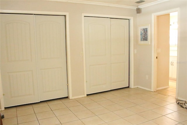 unfurnished bedroom featuring baseboards, visible vents, light tile patterned flooring, multiple closets, and crown molding