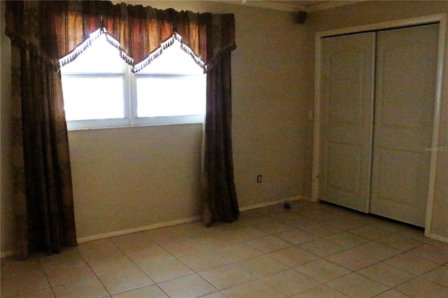 unfurnished bedroom featuring light tile patterned flooring, baseboards, and a closet