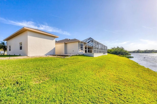 rear view of property with glass enclosure, a lawn, a water view, and stucco siding