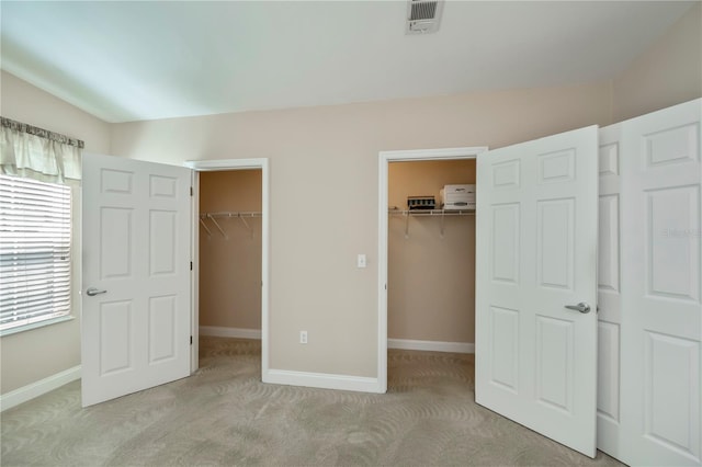 unfurnished bedroom featuring baseboards, a walk in closet, light carpet, and visible vents