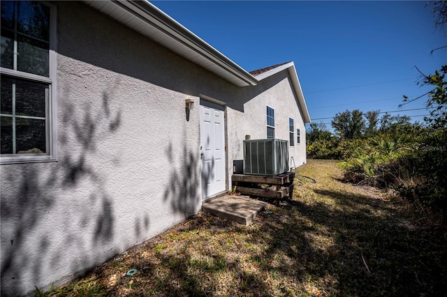 view of side of home with stucco siding, a lawn, and cooling unit