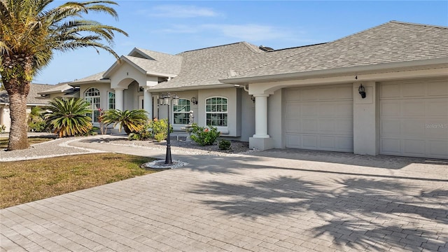 view of front facade with decorative driveway, a garage, roof with shingles, and stucco siding