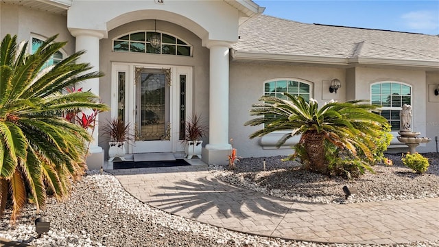 view of exterior entry with stucco siding and roof with shingles